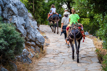 Girl riding a donkey to visit Cave of Diktaion Andron. - obrazy, fototapety, plakaty