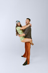 Smiling. Happy young man and woman in stylish retro outfits dancing disco dance isolated over grey...