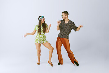 Happiness. Stylish young man and woman in retro outfits emotionally dancing disco dance isolated over grey studio background. 70s fashion, hobby, creativity, hippie lifestyle, American culture