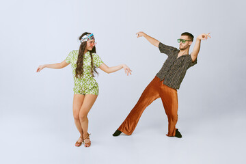 Pretty young girl and handsome man in stylish retro clothes dancing disco dance isolated over grey...