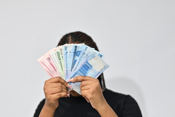 Nigerian woman covering her face with money, showing cash she is about to spend on a white...