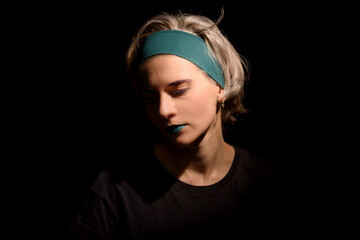 sad blond hair woman with teal lips on black background looking down