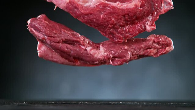 Flying pieces of raw beef steaks falling on table. Filmed on high speed cinema camera, 1000 fps.