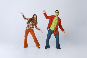 Having fun. Stylish young man and woman in colorful retro outfits dancing disco dance isolated over...