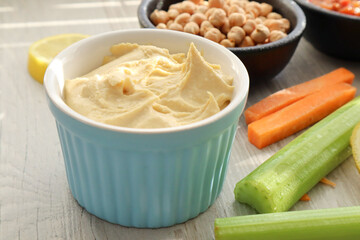 Bowl of hummus with celery sticks and carrot sticks in the foreground 