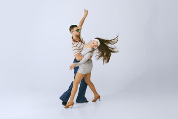 In motion. Young beautiful girl in silver dress and stylish man dancing disco dance isolated over grey studio background. 70s fashion, hobby, creativity, hippie lifestyle, American culture