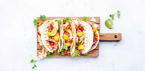 Tacos with grilled chicken, tomato salsa sauce, mango, cilantro and onion in tortilla on cutting...