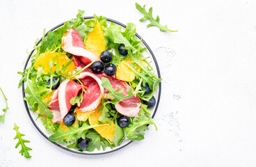 Gourmet salad with smoked duck, oranges, blueberries, arugula and lettuce, white table background, top view
