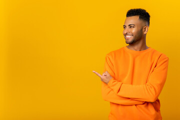 Cheerful indian man pointing at copy space on his finger, showing empty place for idea presentation, product advertising. Indoor studio shot isolated on orange background