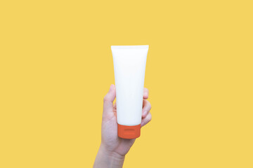 Woman hand holding sunscreen tube over yellow background. Plastic bottle of SPF sunblock cream for...