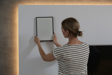 Woman arranging picture frames on wall in new house, diy home improvement concept	