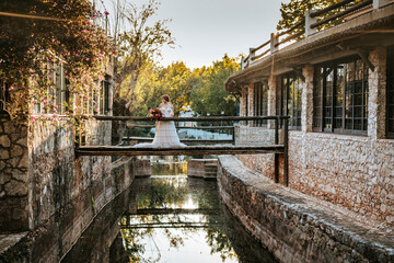 Beautiful bride standing on wooden rustic bridge at sunset time