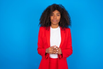 Business Concept - Portrait of young businesswoman with afro hairstyle wearing red over blue background holding hands with confident face.