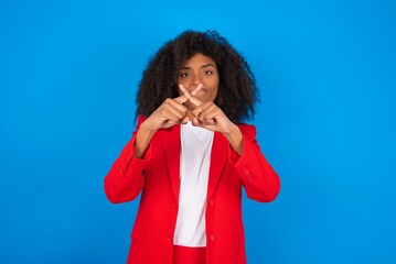 young businesswoman with afro hairstyle wearing red over blue background has rejection angry...