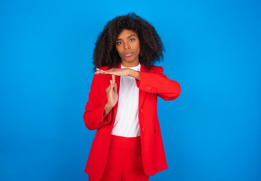young businesswoman with afro hairstyle wearing red over blue background feels tired and bored, making a timeout gesture, needs to stop because of work stress, time concept. - Powered by Adobe