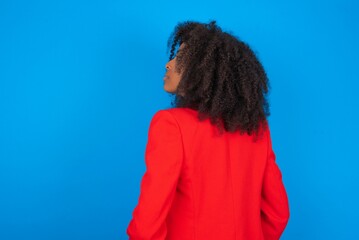 Fototapeta na wymiar The back view of young businesswoman with afro hairstyle wearing red over blue background Studio Shoot.