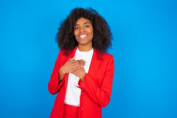 Honest young businesswoman with afro hairstyle wearing red over blue background keeps hands on...