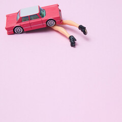 Female legs sticking out from under a pink car, on a pink background with copy space. Minimal pink scene.