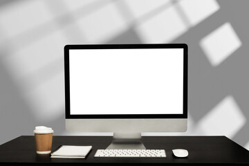 Computer monitor with white blank screen putting on white working desk with wireless mouse and keyboard over blurred modern office as background..