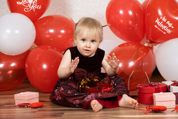 Fototapeta na wymiar A beautiful one and a half years girl on Valentine's Day claps her hands sitting among the balls