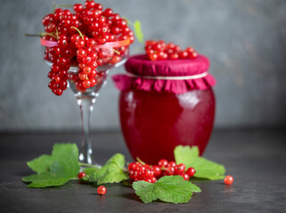 Fresh red currants and a jar of red currant jam on a dark background
