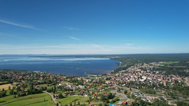 Panoramic View Of A Picturesque Town On The Mountain, On A Beautiful Blue Lake With A Pier. Blue Sky With Mountains And Vast Forests In The Background. High Angle View Of A City With Red Houses