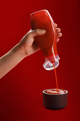 Tomato ketchup concept, a male hand squeezing ketchup bottle and the ketchup pouring in a bowl