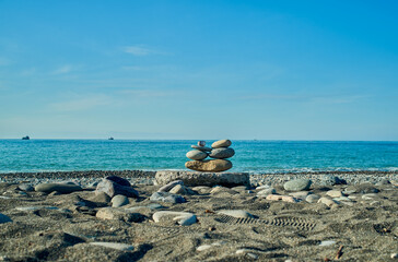 Stones in the form of zen pyramid on the seashore with distant boats in the background