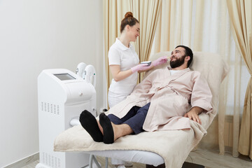 Bearded man getting laser facial treatment by professional cosmetologist in a beauty clinic