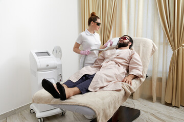 Bearded man getting laser facial treatment by professional cosmetologist in a beauty clinic