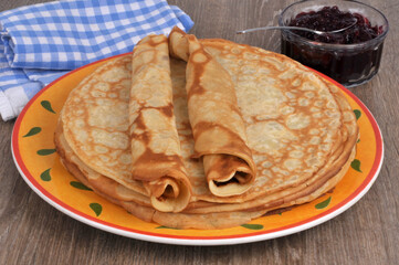 Crêpes roulées posées sur des crêpes dans une assiette avec un ramequin de confiture en gros plan