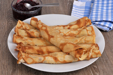 Crêpes roulées posées sur des crêpes dans une assiette avec un ramequin de confiture en gros plan