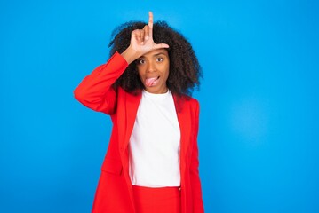 young businesswoman with afro hairstyle wearing red over blue background gestures with finger on...