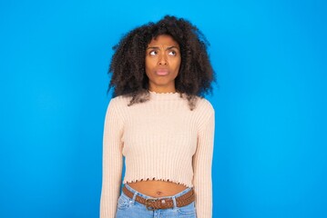 Displeased Young woman with afro hair style wearing crop top over blue background frowns face feels unhappy has some problems. Negative emotions and feelings concept