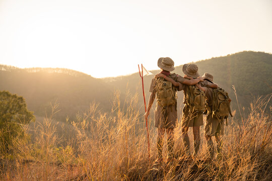 Asian Three Boy Scouts students hiking with backpack stand on the mountain Boy Scouts rejoice at rock climbing success in Scout Camp at sunset.