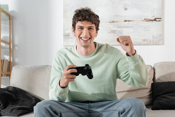 KYIV, UKRAINE - OCTOBER 24, 2022: cheerful young man in sweatshirt playing video game at home
