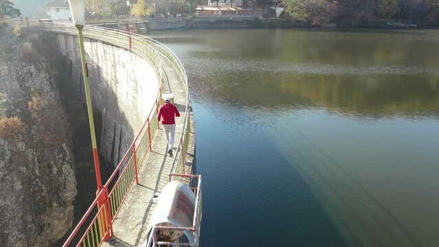 Sport man jogging on the dam crawn, lake bridge in autumn with mountain colorful forest in the background, aerial view