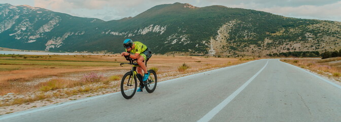 Fototapeta premium Full length portrait of an active triathlete in sportswear and with a protective helmet riding a bicycle. Selective focus 