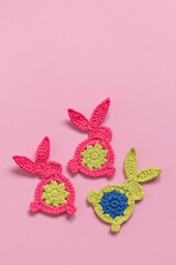 Funny bright crochet Easter bunnies on a pink background. Top view. Copy space.