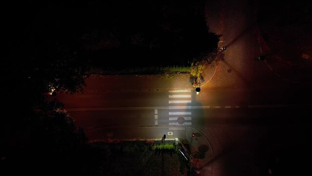 Aerial. A car with its headlights on drives over a pedestrian crosswalk at night. Top view from drone.