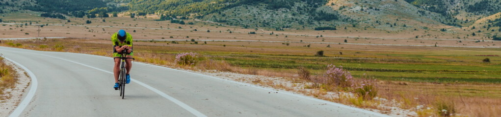 Full length portrait of an active triathlete in sportswear and with a protective helmet riding a bicycle. Selective focus 