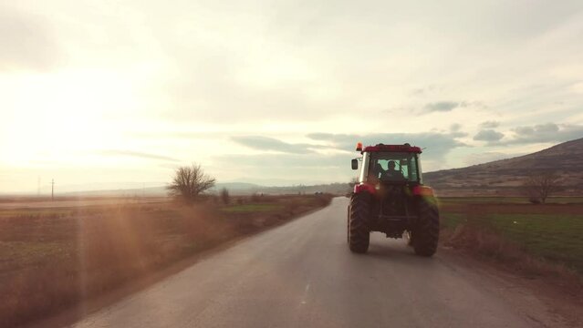 Tractor rides on the asphalt rural road in the sunlight, agriculture fields from the sides