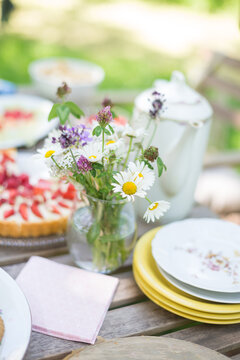 Tisch im Gr&uuml;nen gedeckt mit Erdbeerkuchen und Tellern, einer alten Kaffeekanne und einem Strau&szlig; Wiesenblumen