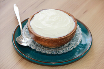 White fermented milk yogurt in a decorative plate with a metal spoon on a wooden background