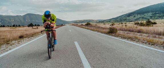 Obraz premium Full length portrait of an active triathlete in sportswear and with a protective helmet riding a bicycle. Selective focus 