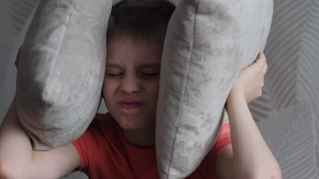 an angry caucasian boy of 8-9 years old covered his ears with pillows and ignores what is happening around. scandals and swearing in the family involving children.