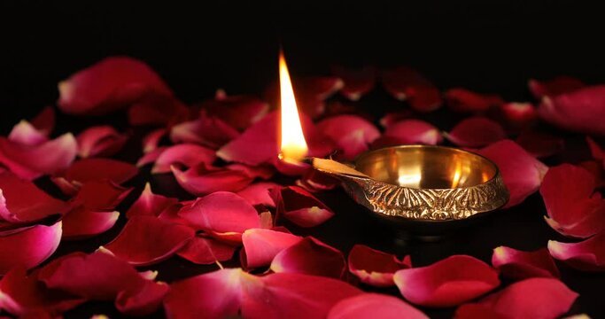 Decorative Diya lamp. Oil lamp burning on rose petals decoration - Diwali festival. Decorative rose petals with Puja Diya lighted with bright flame.