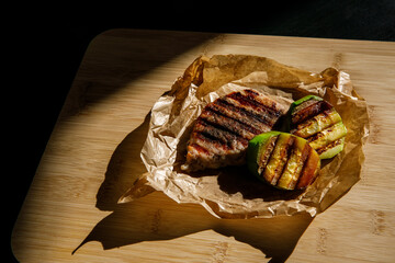 two grilled pork steaks and zucchini in craft paper on a wooden background