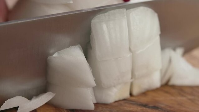 Knife cuts white onion into square pieces