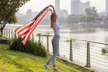 Patriotic holiday. Happy young stylish caucasian woman with American flag outdoors on sunset. USA...